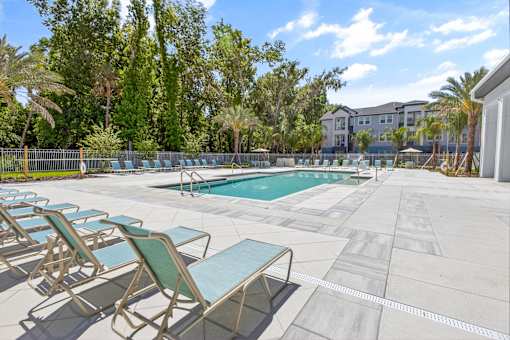 A pool surrounded by trees and chairs.