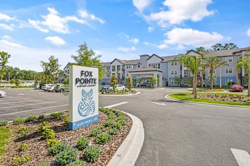A sign for Fox Pointe Apartments stands in front of a parking lot and apartment buildings.
