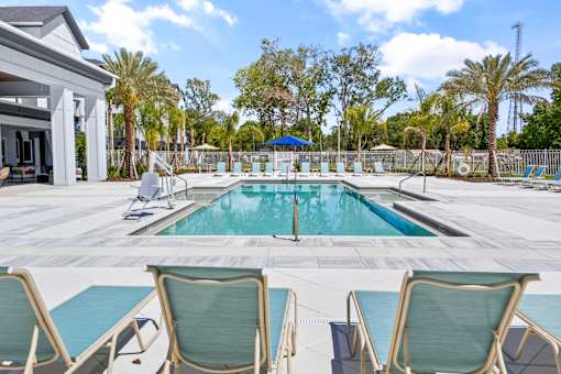 A pool surrounded by chairs and trees.