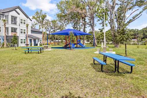 A playground with a blue canopy and a picnic table is surrounded by a grassy area.