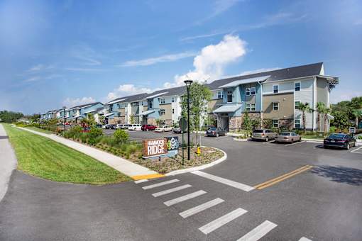 A sunny day at the Hamance Ridge apartment complex with cars parked and driving.