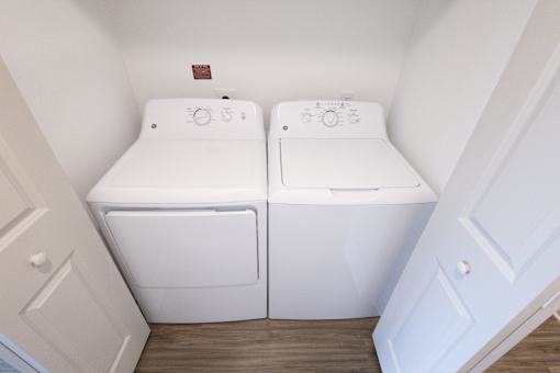 A pair of white front loading washing machines in a small laundry room.