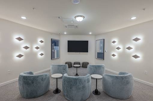 A room with grey chairs and a black television mounted on the wall.
