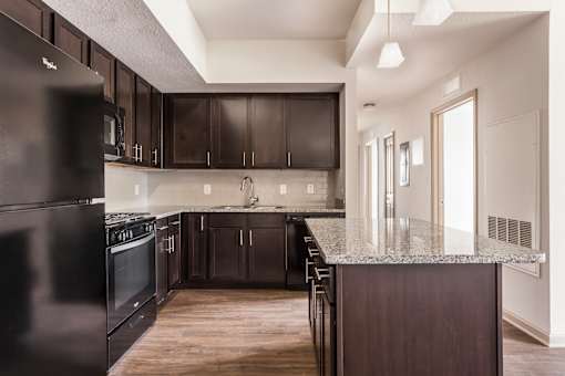 A kitchen with dark wood cabinets and a black refrigerator.