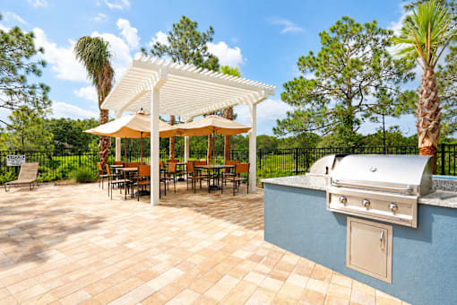 A white pergola is over a table with chairs and a grill is on the side.