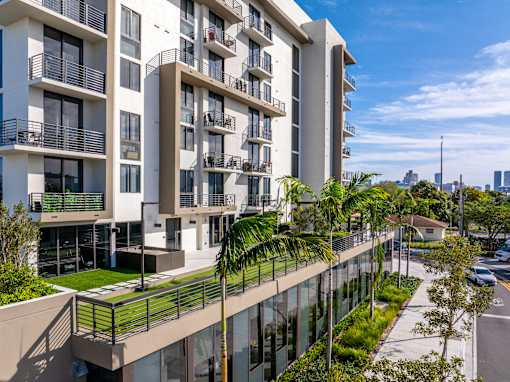 A modern apartment building with balconies and palm trees in front.