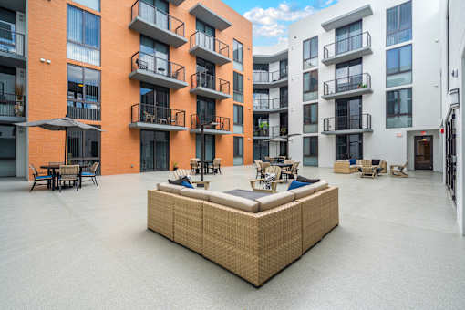 A large wicker sofa sits in the middle of a courtyard with buildings in the background.
