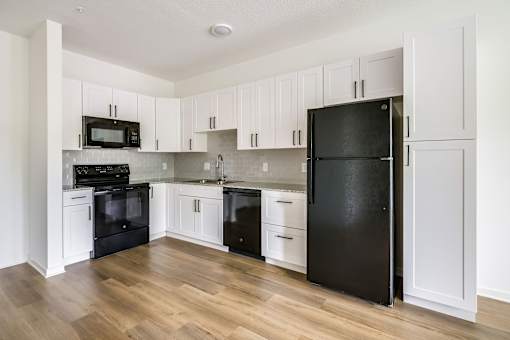 A black refrigerator stands in a kitchen with white cabinets.