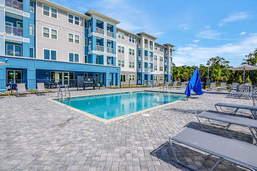A large swimming pool is surrounded by a patio with lounge chairs and umbrellas.