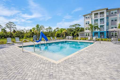 A swimming pool surrounded by a brick patio and a blue umbrella.