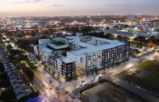 A modern building with a green roof is lit up at night with a cityscape in the background.