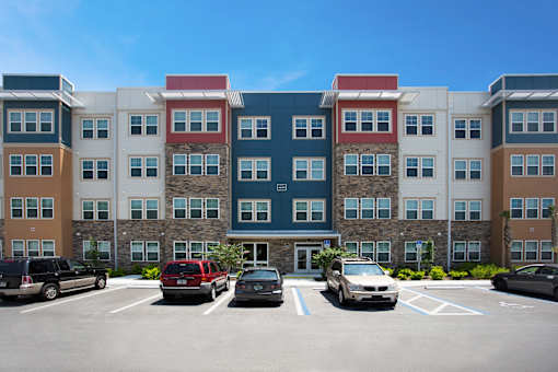 A parking lot with cars and a multi-story building with red, white, and blue sections.