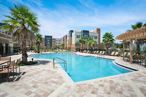 A pool surrounded by palm trees and lounge chairs.