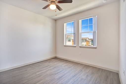 A room with a ceiling fan and two windows.