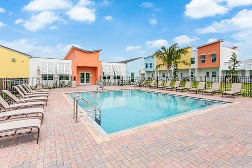 a swimming pool with chairs and buildings in the background