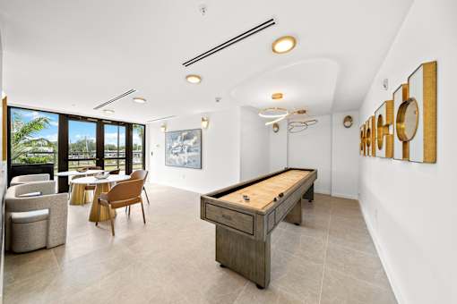 A billiard table is in the middle of a room with a white ceiling and a painting hangs on the wall.