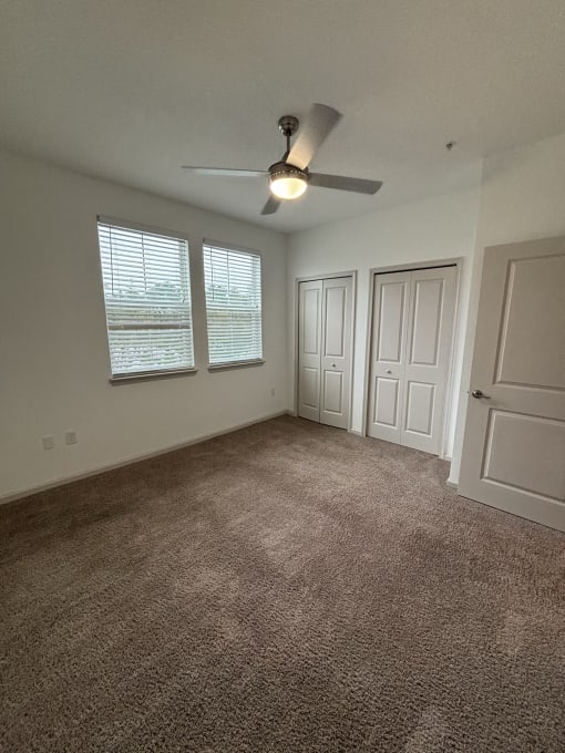 an empty living room with a ceiling fan and two windows