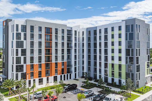 A modern multi-story building with a parking lot in front.