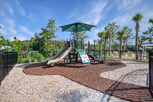 A playground with a green umbrella and a slide.
