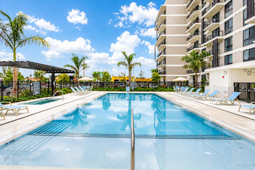 A large swimming pool with sun loungers and a building in the background.