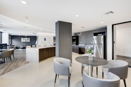 a room with a table and chairs and a kitchen in the background