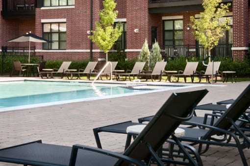 a pool with chaise lounge chairs and a brick building in the background  at The Sheffield Englewood, Englewood, NJ