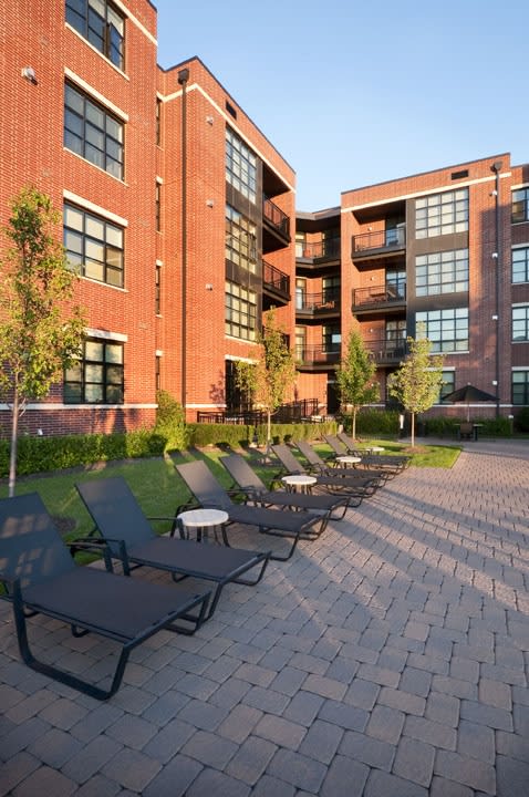 a courtyard with chaise lounge chairs and trees in front of a large brick building  at The Sheffield Englewood, New Jersey