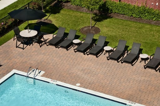 an aerial view of a pool and patio with black lounge chairs and umbrellas  at The Sheffield Englewood, Englewood