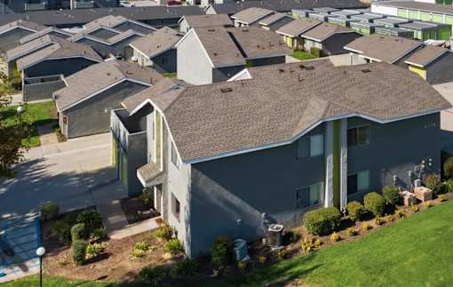 A large grey house with a brown roof and a green lawn in front.