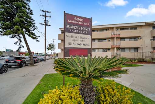 A palm tree stands in front of a sign for Academy Pointe Apartments.