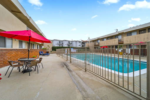 A pool area with a table and chairs and a red umbrella.