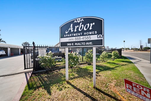A sign for Arbor Apartment Homes is displayed in front of a fence.