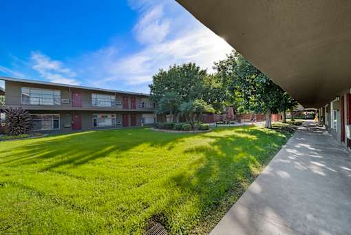 A long concrete walkway leads through a grassy area in front of apartment buildings.