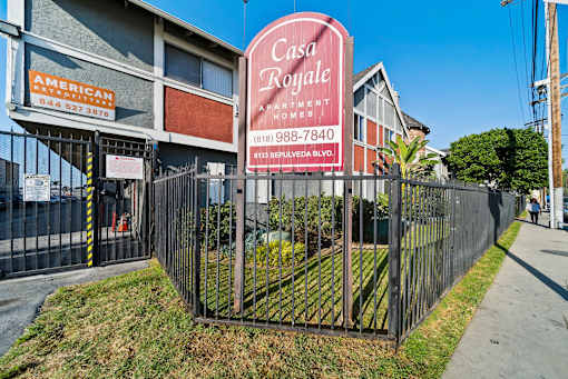 A sign for Casa Royale Apartments is displayed in front of a fence.