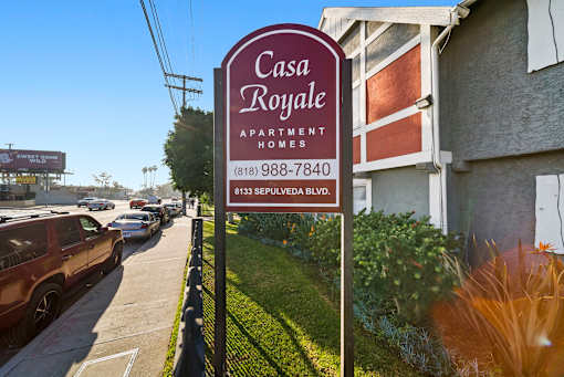 A sign for Casa Royale Apartment Homes stands on a sidewalk.