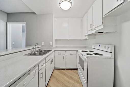 A white kitchen with a stove, sink, and cabinets.