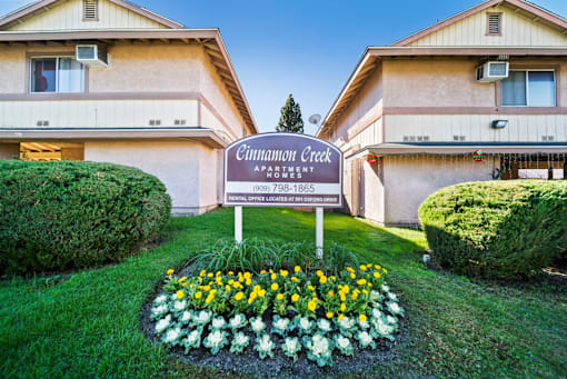 A sign for Cinnamon Creek Apartment is in the foreground of a grassy area.