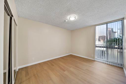 Empty room with wooden floor and sliding glass door.