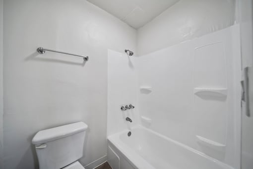 A white bathroom with a toilet, a bathtub, and a towel rack.