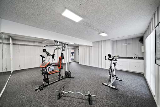 A gym with a variety of equipment including a stationary bike, a rowing machine, and a weight bench.