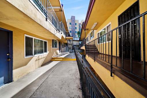 A long, narrow balcony with black railings and a yellow wall.