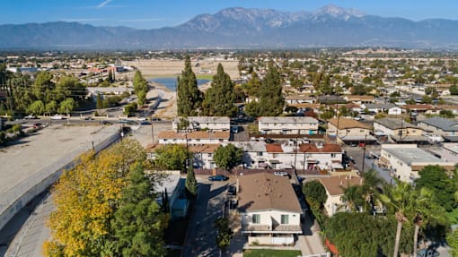A residential area with houses and trees in the foreground and mountains in the background.