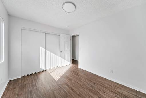 A room with white walls and wooden flooring with a door and a window.