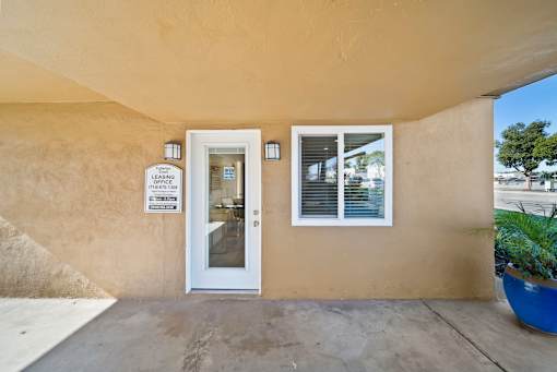 A beige building with a white door and a sign on the wall.