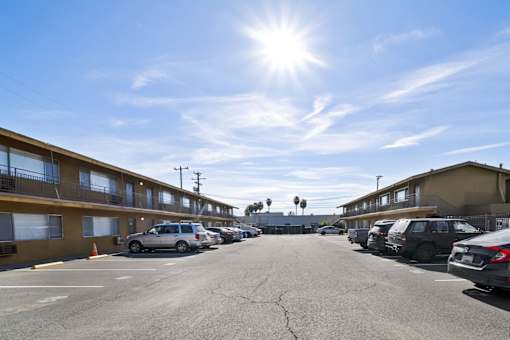 A sunny day at a parking lot with cars parked and buildings in the background.