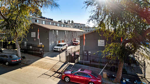 A red car is parked in front of a building with a black fence.
