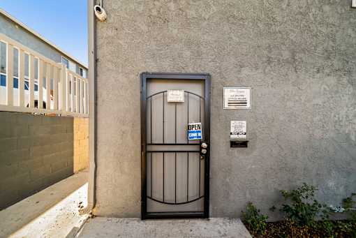 A black gate with a blue sign that says "OPEN" in front of a grey wall.