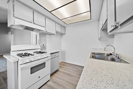A white kitchen with a stove, sink, and cabinets.
