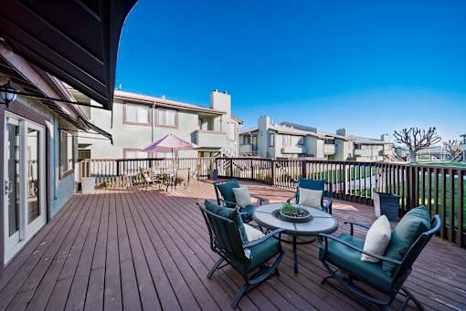 A wooden deck with a table and chairs overlooking a row of houses.