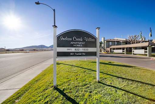 A sign for Indian Creek Village Apartment Homes stands on a grassy area by a road.